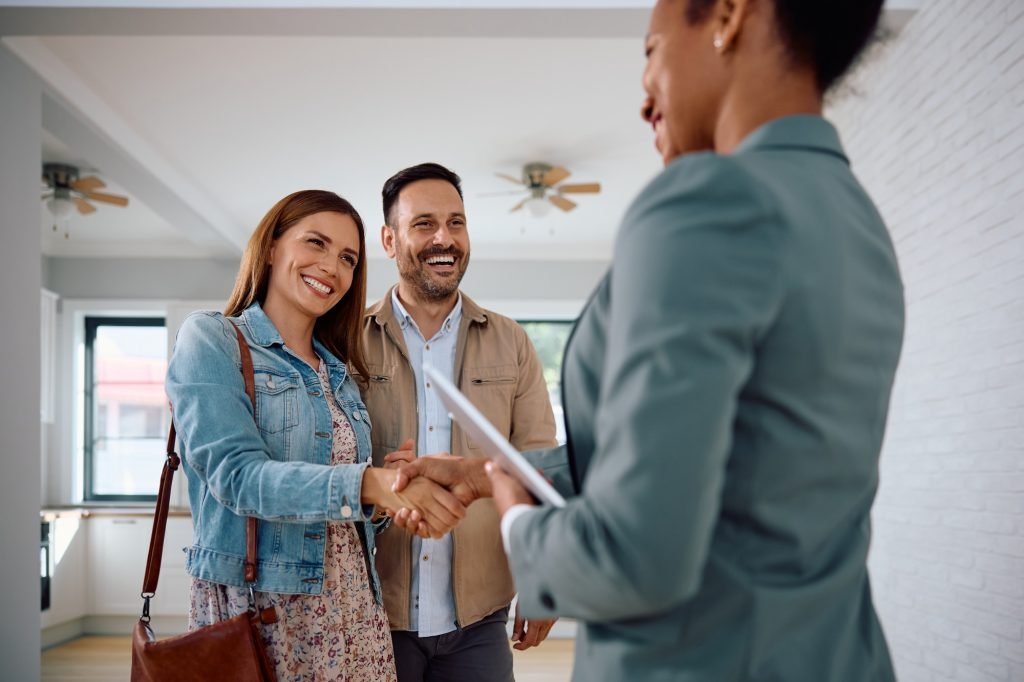 Happy couple of real estate buyers handshaking with their agent in a new house.